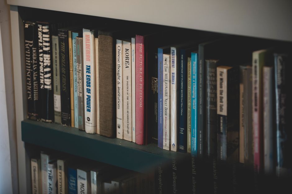 A collection of books displayed on a sunlit bookshelf inside a glass enclosure.