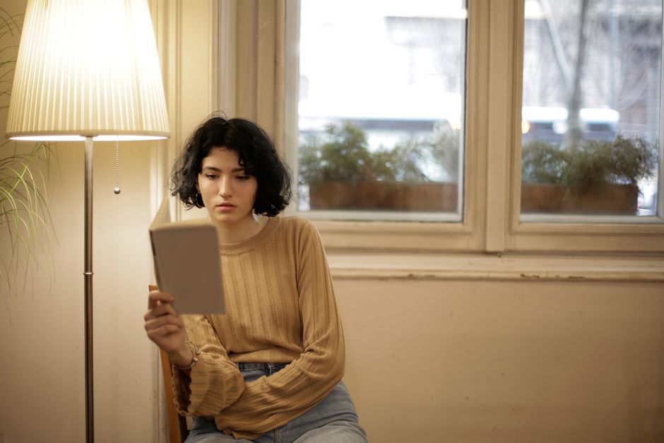 Side view of clever female with stylish haircut relaxing with book on window in daytime